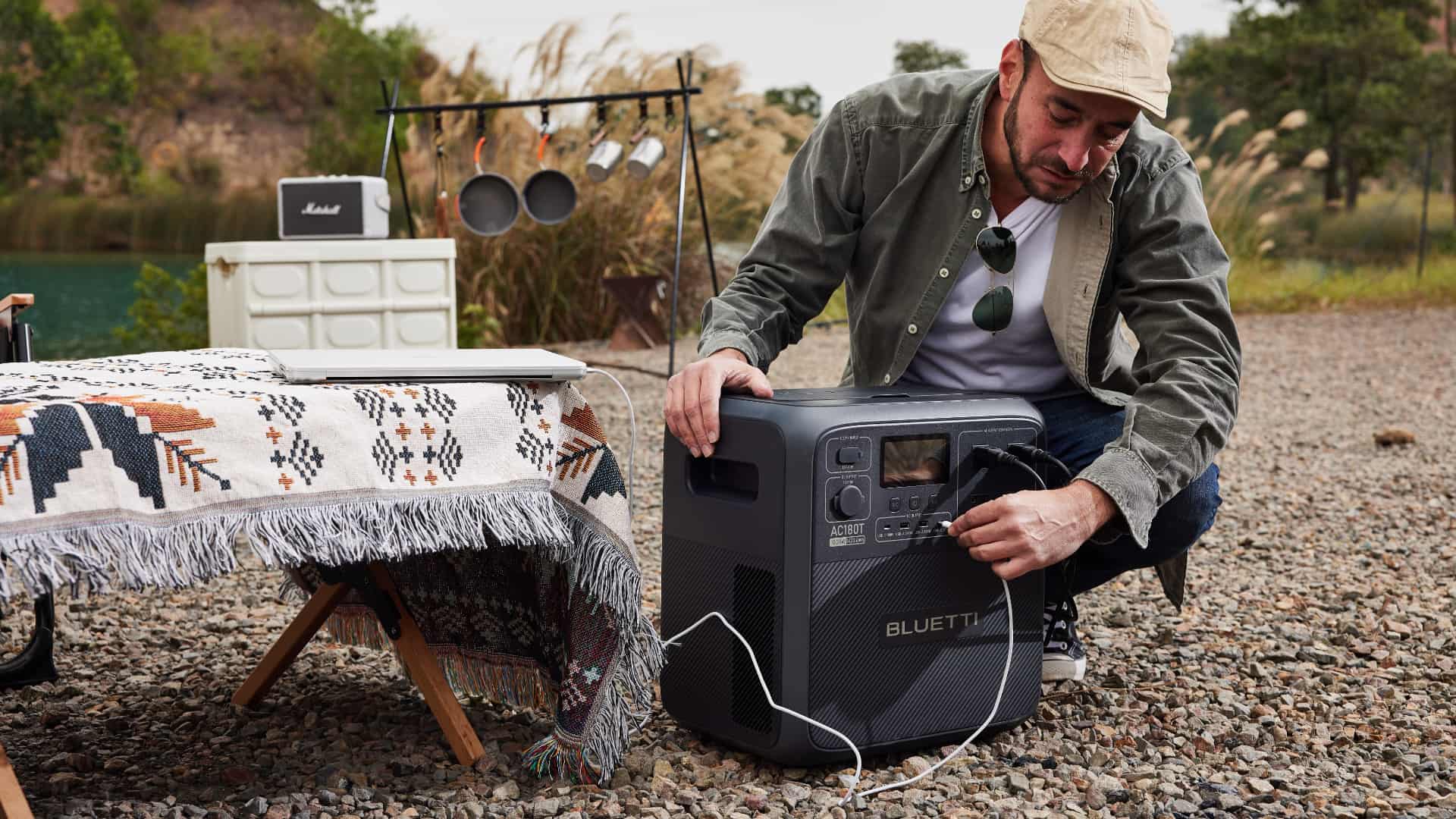 Man camping in the wilderness, plugging his laptop into a USB-C port of Bluetti's AC180T portable power station 
