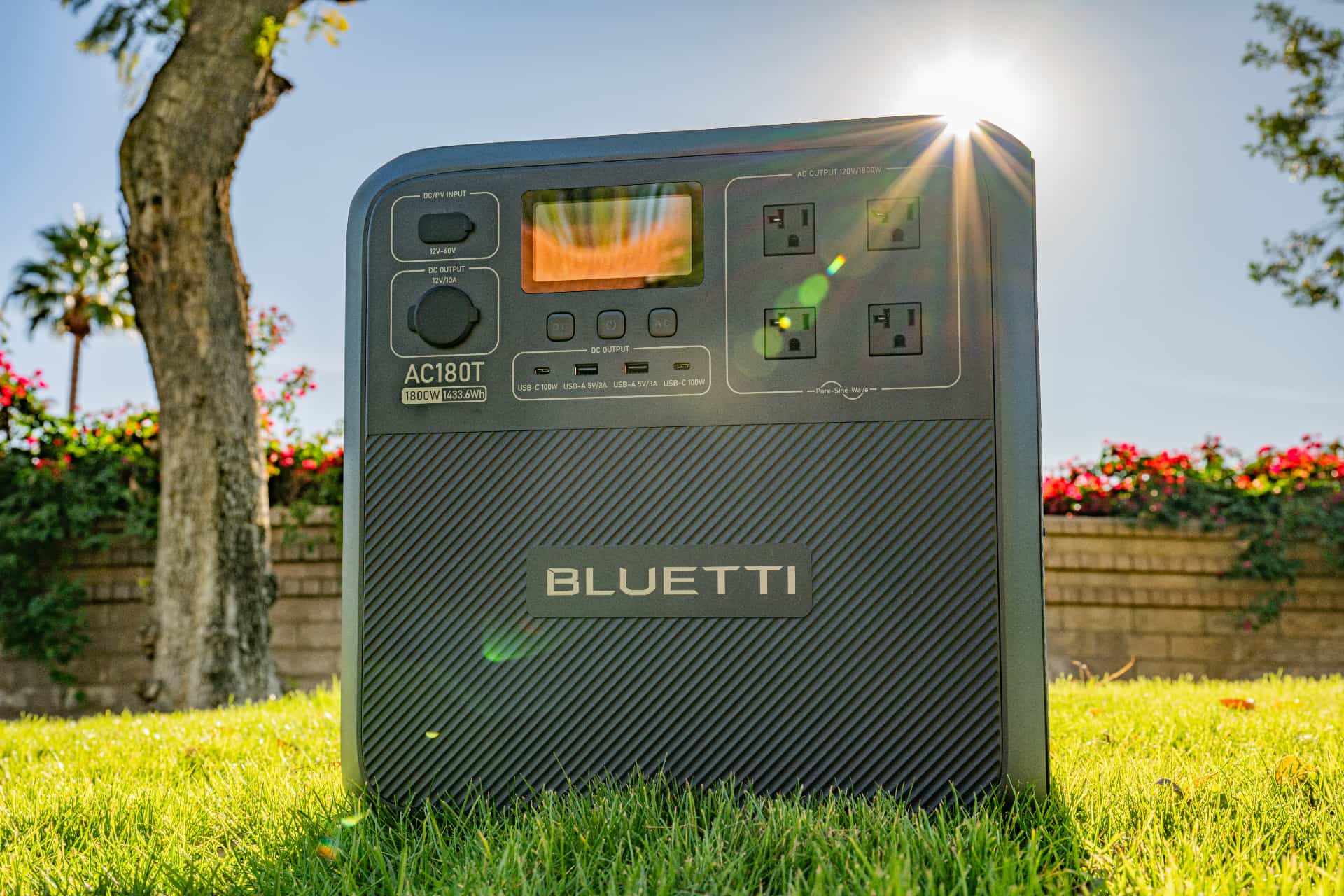 Bluetti's AC180T portable power station on the grass under direct sunlight, showcasing its outlets and ports