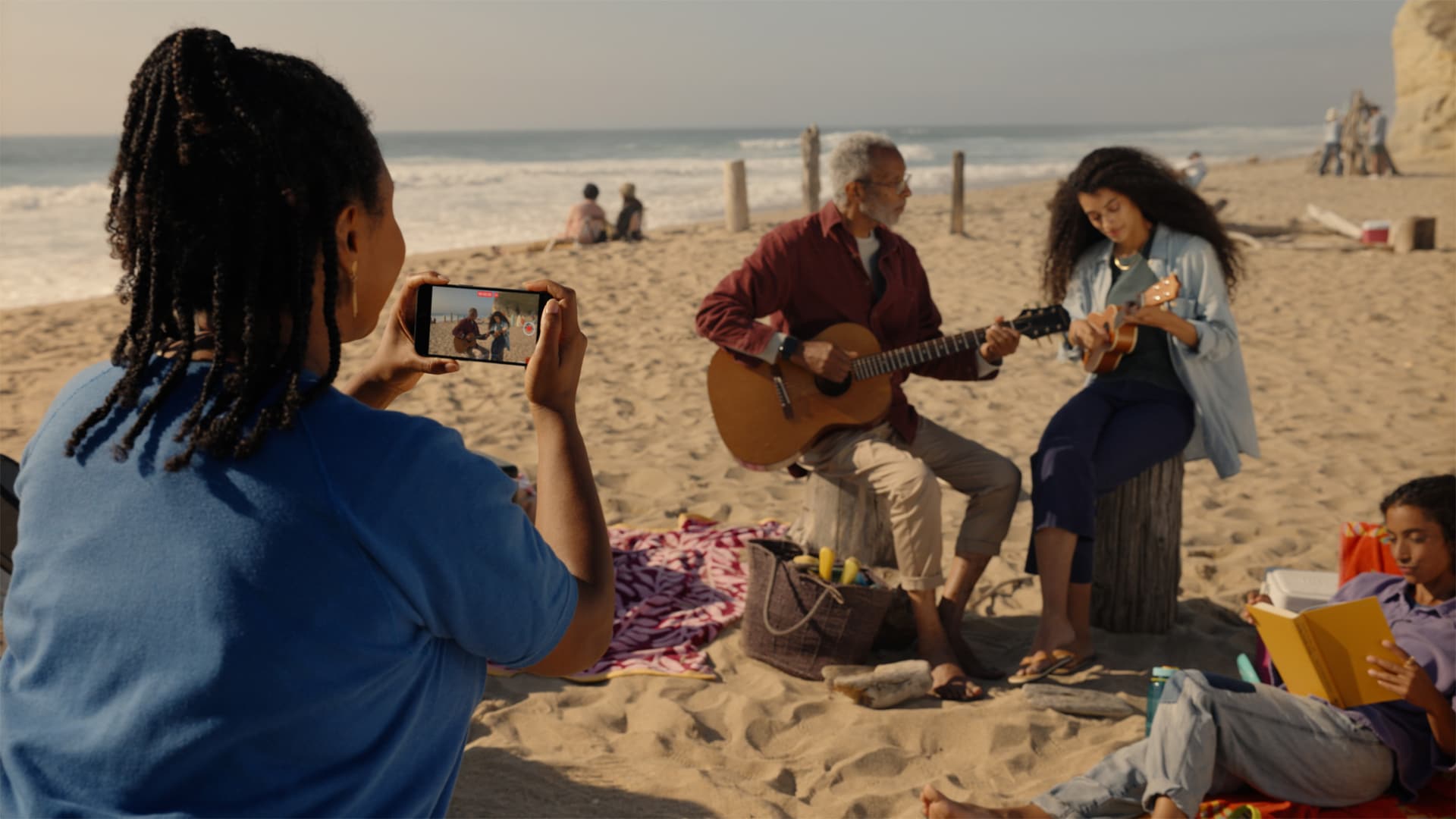 Woman on the beach using her iPhone to capture a spatial video of an older man and woman playing guitars